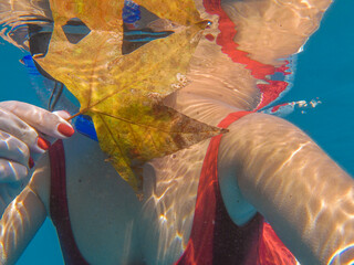 Young woman taking a selfie underwater wearing an underwater mask with a maple leaf in a red swimsuit in autumn.