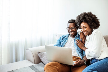 Attractive couple using laptop together on sofa to shop online at home in the living room. Attractive couple using laptop together on sofa at home in the living room