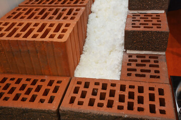 A close-up of cross-section of an unfinished energy efficient, thermal insulated house wall built from porous ceramic blocks, polystyrene, and exterior alleviation exposed bricks.