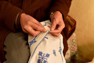 gros plan sur les mains d'un homme faisant de la broderie sur un tissus blanc 