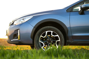 Close up of blue off road car on green grass. Traveling by auto, adventure in wildlife, expedition or extreme travel on a SUV automobile. Offroad 4x4 vehicle in field at sunrise.