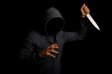 aggressive young man in a hood swinging a knife with a knife, face not visible on black background.