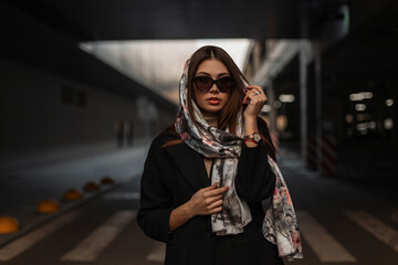 luxurious attractive young woman with sexy lips with stylish silk scarf on head in trendy black coat