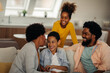 © bernardbodo - Afro parents and their children are socializing while sitting on the sofa in the living room