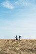 © Ivan Acedo - A couple with their dog walking towards the horizon in a field with blue sky
