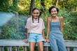 © Inti St. Clair - Portrait of smiling teen sisters sitting on bridge railing in nature park