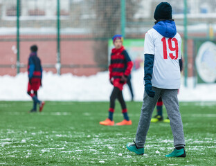 Wall Mural - Boys in white sportswear running on soccer field with snow on background. Young footballers dribble and kick football ball in game. Training, active lifestyle, sport, children winter activity