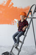 © Andrii Lysenko - boy dressed in protective orange sits on a construction ladder.