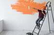 © Andrii Lysenko - a boy dressed in protective orange sits on a construction ladder points with a roller to an empty space for text.