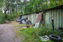 View Of The Old Abandoned Barns Near Which Litter Debris And Tires In The Background Of The Forest, Copy Space