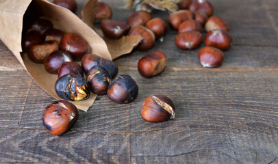 Wall Mural - roasted chestnuts  in a papaer bag spilled on wooden table