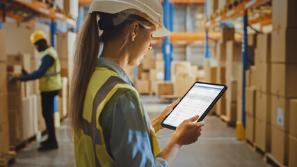 Wall Mural - Professional Female Worker Wearing Hard Hat Uses Digital Tablet Computer with Inventory Checking Software in the Retail Warehouse full of Shelves with Goods. Delivery, Distribution Center.