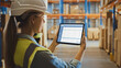 © Gorodenkoff - Professional Female Worker Wearing Hard Hat Uses Digital Tablet Computer with Screen Showing Inventory Checking Software in the Retail Warehouse full of Shelves with Goods. Over the Shoulder View