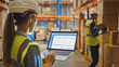 © Gorodenkoff - Professional Female Worker Wearing Hard Hat Holds Laptop Computer with Screen Showing Inventory Checking Software in the Retail Warehouse full of Shelves with Goods. Over the Shoulder Side View