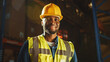 © Gorodenkoff - Handsome and Happy Professional Worker Wearing Safety Vest and Hard Hat Charmingly Smiling on Camera. In the Background Big Warehouse with Shelves full of Delivery Goods. Medium Close-up Portrait
