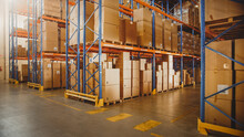 Large Retail Warehouse Full Of Shelves With Goods In Cardboard Boxes And Packages. Logistics, Sorting And Distribution Facility For Further Product Delivery.