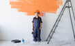 © Andrii Lysenko - a boy dressed in overalls and a protective helmet stands near the wall holding a brush in his hands. Home renovation concept.