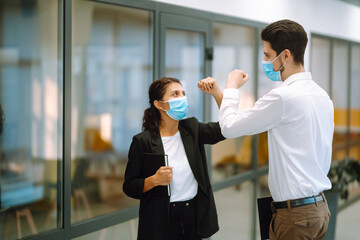 Two manager in protective medical masks bumping elbows while greeting each other in in modern office. Business partners handshake during coronavirus. Covid-19.