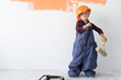 © Andrii Lysenko - a little boy dressed in an orange helmet on his head is standing near the wall straightens a large jumpsuit.