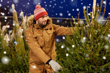 Canvas Print - winter holidays, sale and people concept - happy smiling man buying christmas tree at street market in evening over snow