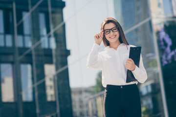 Sticker - Photo of pretty smiling young woman wear white formal shirt arm hand spectacles holding clipboard outdoors