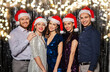 © Syda Productions - celebration, people and holiday concept - happy friends in santa hats at christmas party over foil fringe and garland lights on background