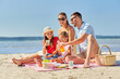 © Syda Productions - family, leisure and people concept - happy mother, father and two daughters having picnic on summer beach and drinking juice