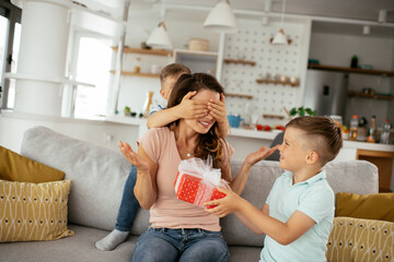 two young sons are giving their mother a gift. mother is suprised to receive a present from sons.