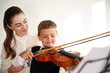Young woman teaching little boy to play violin indoors