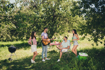 Poster - Full length photo of four happy friends weekend party hold beer bottle play guitar chill conversation outside in outdoors backyard