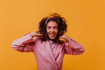 Amazing black girl expressing positive emotions during photoshoot on orange background. Studio photo of relaxed blithesome woman wears pink clothes.