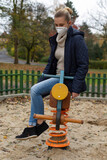 Fototapeta Tęcza - young woman with respirator sitting on children toy on abandoned playground during quarantine and lockdowm due to covid-19