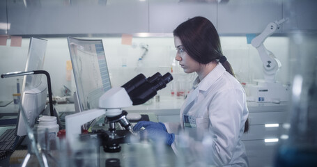 Wall Mural - young female doctor working with microscope. close up on face. futuristic laboratory interior