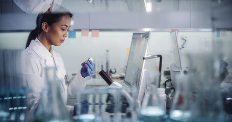 Wall Mural - asian female doctor working in futuristic laboratory. using microscope and computer for blood sample