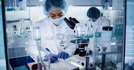 Wall Mural - female science team working on biohazardous samples. using microscope and computer with data