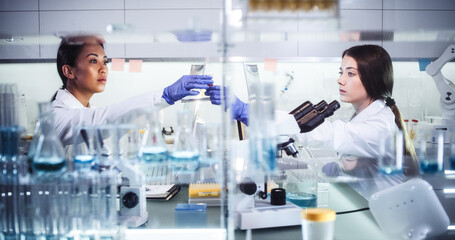 Wall Mural - female doctors testing samples in futuristic laboratory. using microscopes and computer with data