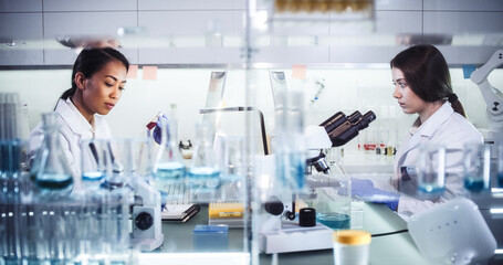 Wall Mural - female doctors testing samples in futuristic laboratory. using microscopes and computer with data