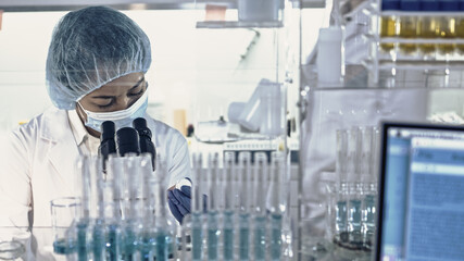 Wall Mural - asian female doctor working with biohazardous samples. using microscope in futuristic laboratory