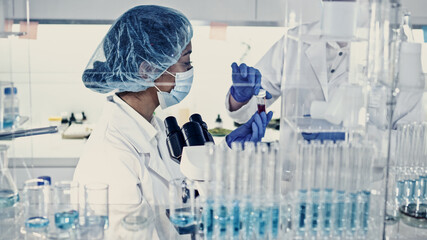 Wall Mural - asian female doctor working with biohazardous samples. using microscope in futuristic laboratory