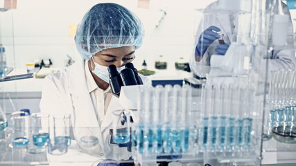 Wall Mural - asian female doctor working with biohazardous samples. using microscope in futuristic laboratory