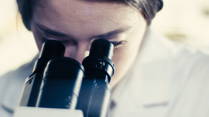 Wall Mural - young female doctor working with microscope. close up on face. futuristic laboratory interior