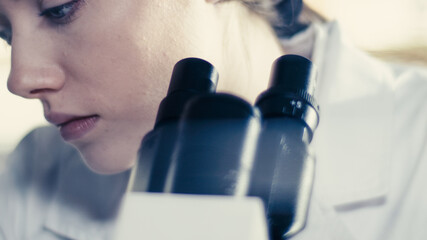 Wall Mural - young female doctor working with microscope. close up on face. futuristic laboratory interior