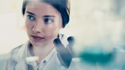 Wall Mural - young female doctor working with microscope. close up on face. futuristic laboratory interior