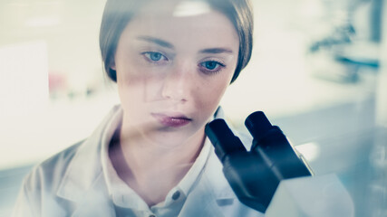 Wall Mural - young female doctor working with microscope. close up on face. futuristic laboratory interior