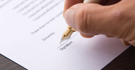 Wall Mural - A hand signing a letter. Hand holding a pen and signing a document.