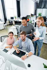 Smiling multicultural businesspeople using graphics tablet and computer while working together in office