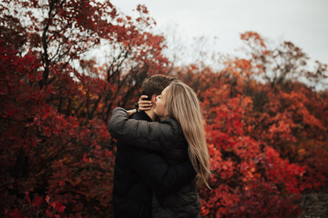 Wall Mural - Side view of a lovely young happy couple embracing in colourful red autumn park. 