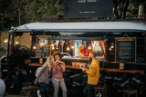 Fototapeta Panele - multiethnic group of  people socializing while eating outdoor in front of modified truck for fast food