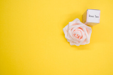 Poster - Top view of a rose tea essential oil next to a beautiful pink rose on a yellow surface