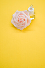 Poster - Vertical shot of essential oil next to a beautiful pink rose on a yellow surface